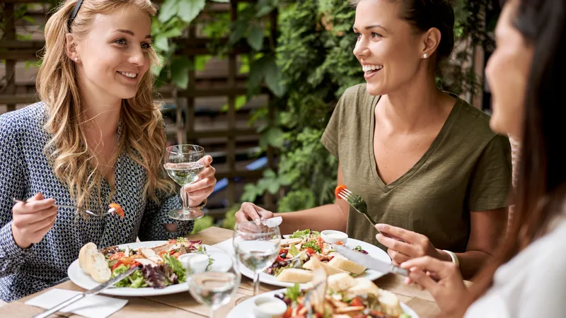 Drei Freundinnen sitzen im Restaurant, essen und unterhalten sich lächelnd