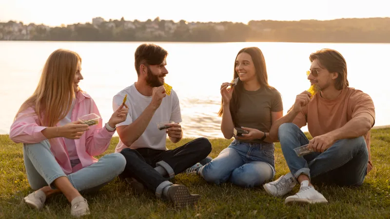 Vier Freunde sitzen am See bei Sonnenuntergang und essen Snacks