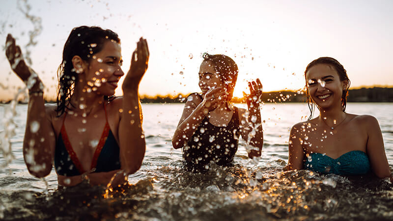 Drei Freundinnen plantschen bei Sonnenuntergang lachend im Wasser