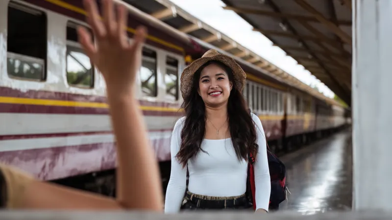 Junge Frau am Bahnsteig lächelt freudig, als sie ihre winkende Freundin sieht