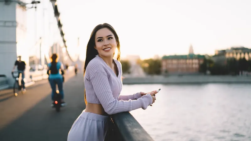 Junge Frau steht auf der Brücke mit Smartphone und wartet lächelnd auf Freunde
