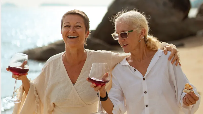 Zwei Freundinnen spazieren arm in Arm mit Wein am Strand