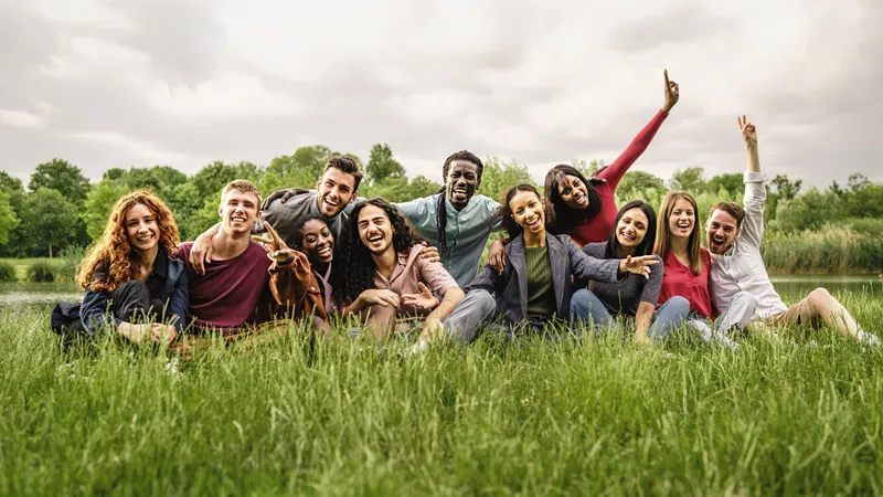 Elf junge Freund:innen sitzen in einer Wiese und schauen lachend in die Kamera