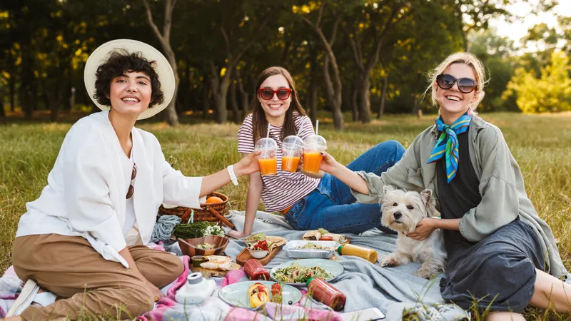 Drei Freundinnen mit Hund beim Picknick im Park