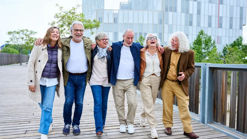 Sechs Senioren gehen Arm in Arm und lachend eine Holzbrücke entlang