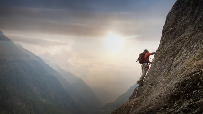 Mann klettert den Berg hinauf, hinter ihm der Sonnenuntergang