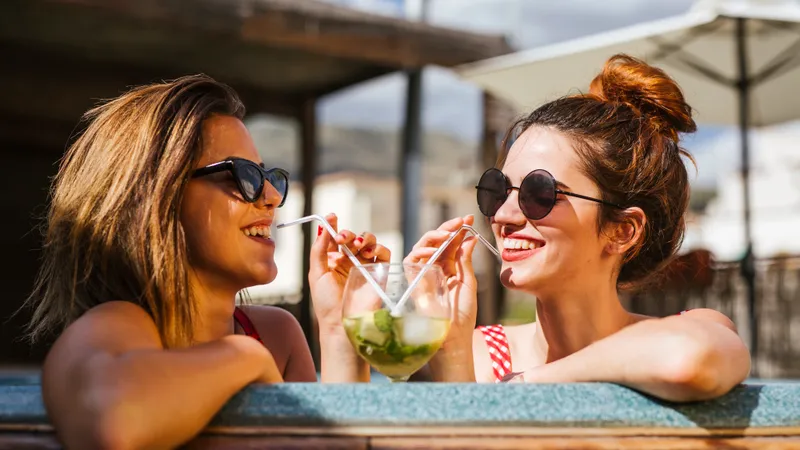 Zwei Freundinnen trinkenlachend einen Cocktail im Pool