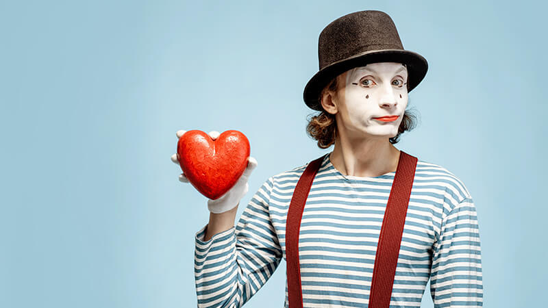 Scammer mit Clown Maske Hut und Herz in der Hand