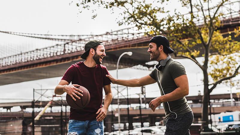 Ein junger Mann greift seinem Basketball-Partner freundschaftlich und lachend auf die Schulter
