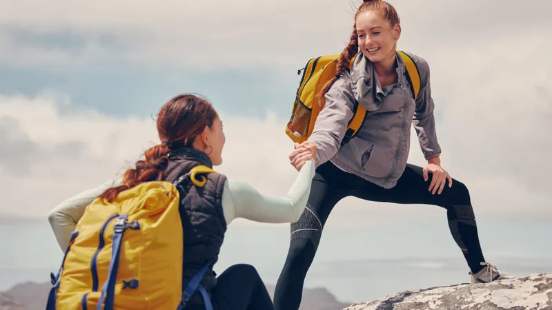 Junge Frau hilft freundin beim Wandern den Hang hinauf