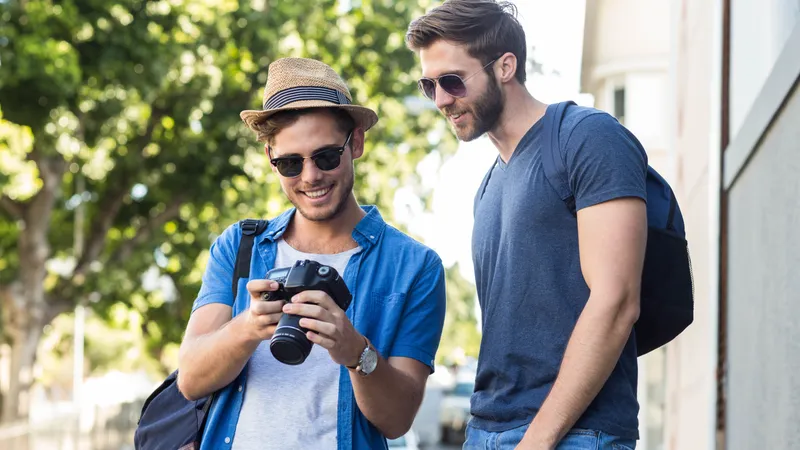 Zwei Reisende mit Sonnenbrille betrachten ein Foto auf einer Kamera, die die Person links in der Hand hält.