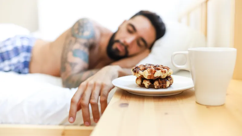 Mann schläft im Bett, auf seinem Nachttisch warten Waffeln und Kaffee