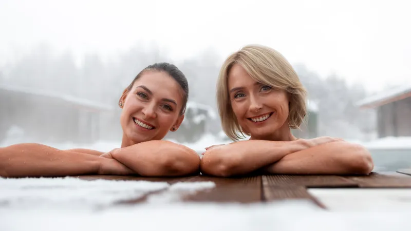 Zwei Freundinnen lachen aus dem warmen Außenpool, rundherum liegt Schnee