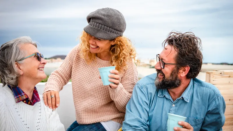 Drei Freunde mittleren Alters sitzen draußen lächelnd beisammen und trinken Kaffee