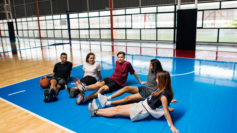 Fünf junge Freunde sitzen am Boden der Sporthalle im halbkreis und unterhalten sich