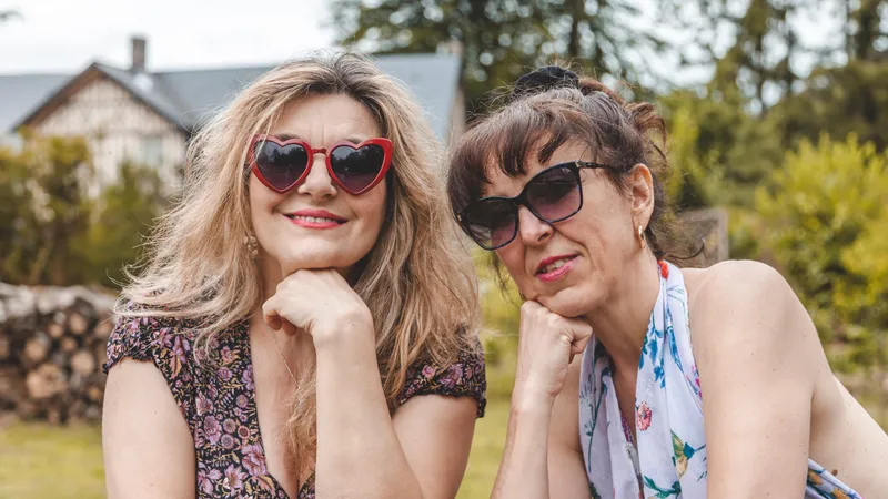 Zwei Freundinnen in Sommerkleidern und mit Sonnenbrillen sitzen im Garten