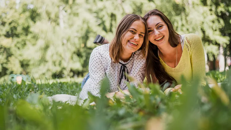 Zwei Freundinnen liegen im Gras und lächeln in die Kamera