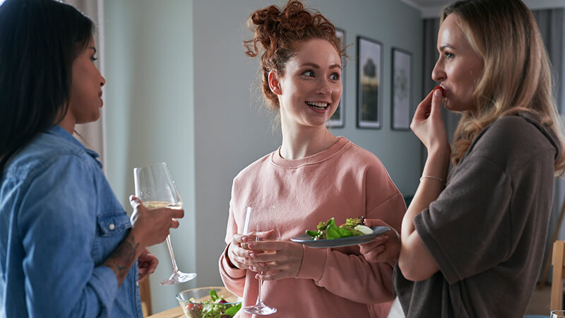 Drei Frauen unterhalten sich in der Küche, trinken Wein und essen Salat
