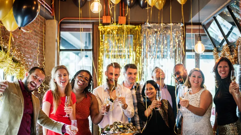 Zehn chic gekleidete Freund:innen feiern Silvester, über ihnen schweben edle Luftballone und die Fenster sind mit goldenen Girlanden dekoriert.