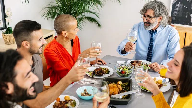 Freunde unterschiedlichen Alters sitzen lächelnd am gedeckten Esstisch