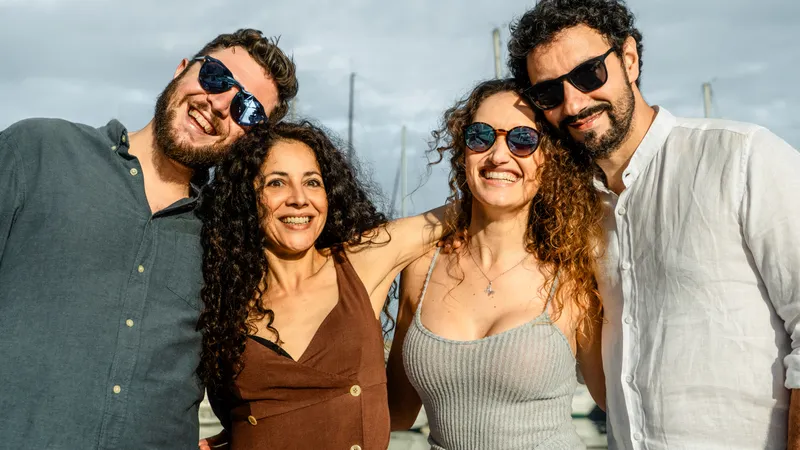 Vier Freunde posieren lächelnd und Arm in Arm mit Sonnenbrillen am Gesicht