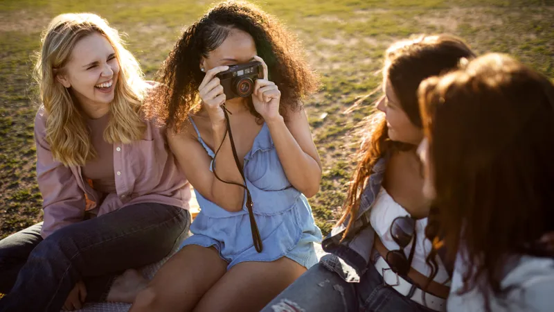 Junge Frau macht Foto ihrer Freundinnen mit einer Kamera im Park