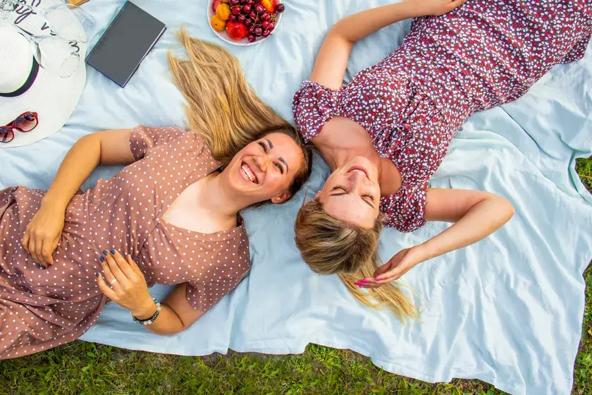 Zwei Freundinnen liegen lachend auf einer Picknickdecke